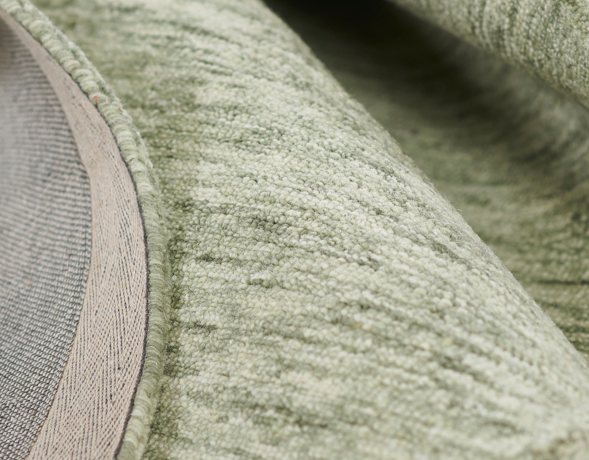 Close-up of sage green plush rug with soft loop pile and beige edging.
