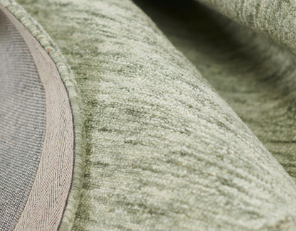 Close-up of sage green plush rug with soft loop pile and beige edging.