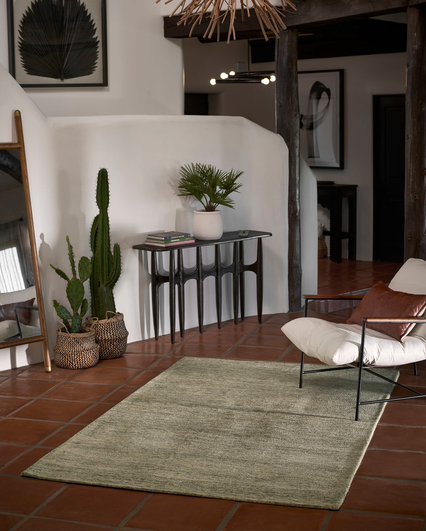 Sage-green rug runner in a boho living room with terracotta tiles, metal-framed lounge chair, console table, & potted cacti.