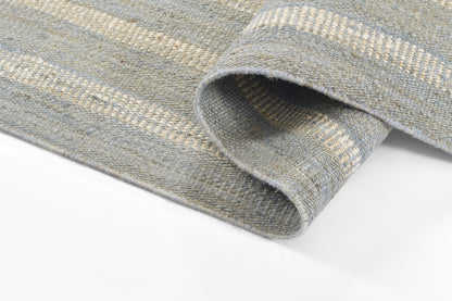 Blue-gray striped woven rug with thick textured weave, rolled edge visible; versatile for living room or bedroom.