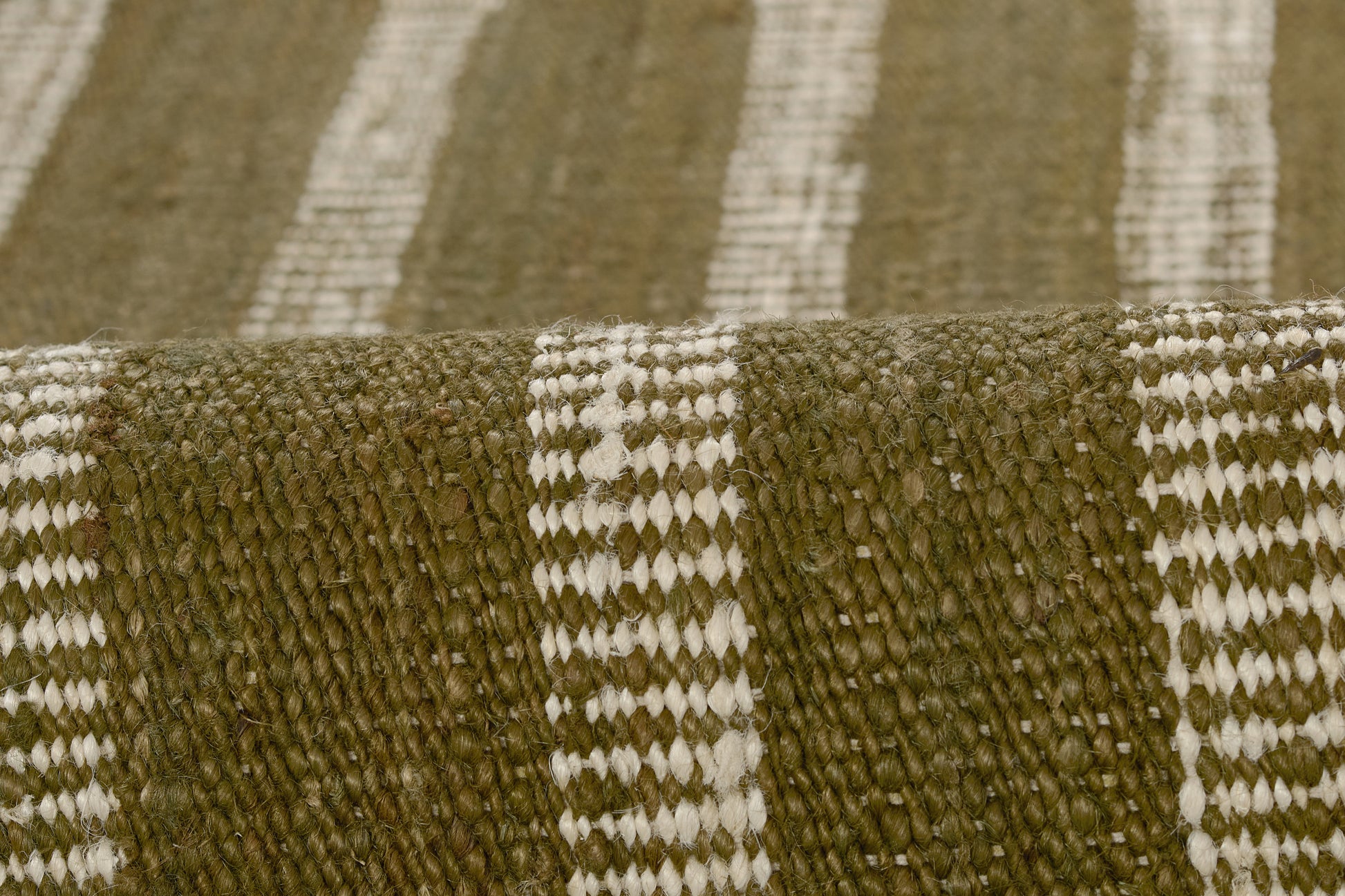 Close-up of olive green and cream striped woven rug with chunky fibers and rolled edge.