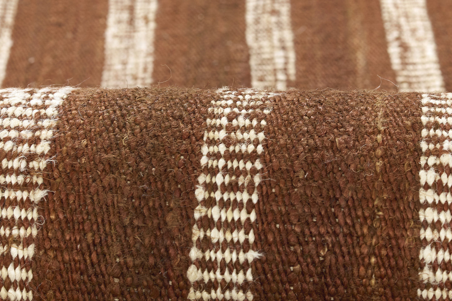 Brown woven rug with white stripes, chunky textured fabric close-up.