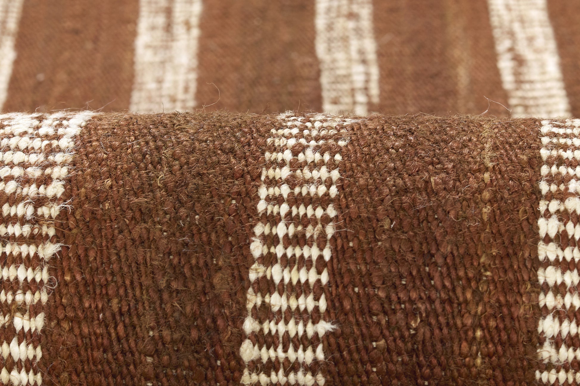 Brown woven rug with white stripes, chunky textured fabric close-up.