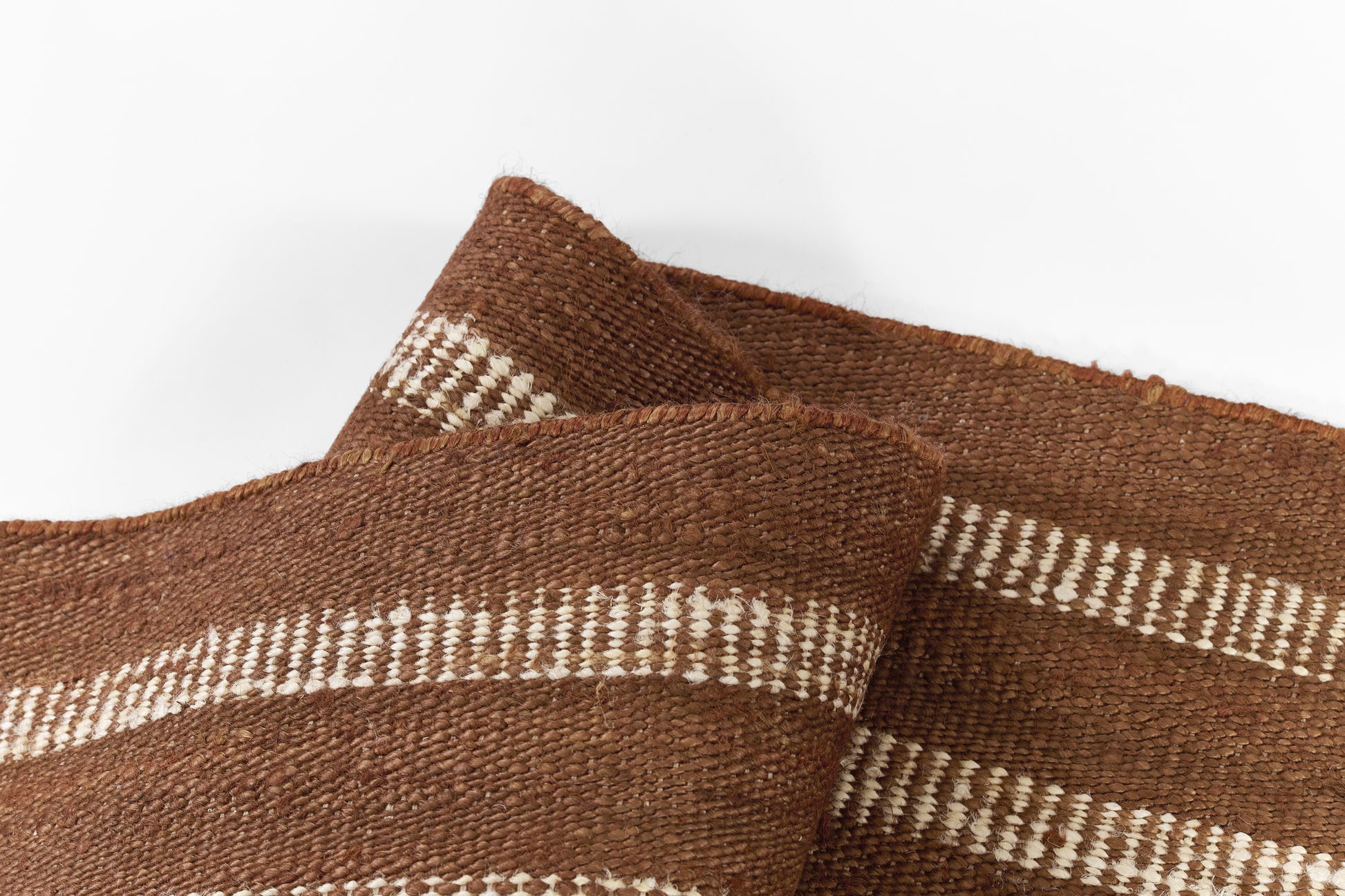 Close-up of brown woven rug fabric with white horizontal stripes; rustic, jute-like texture.