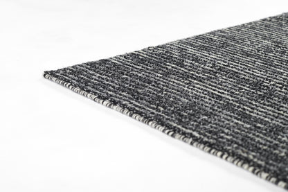 Close-up of a black and gray woven rug with a textured striped surface and a striped edge binding.
