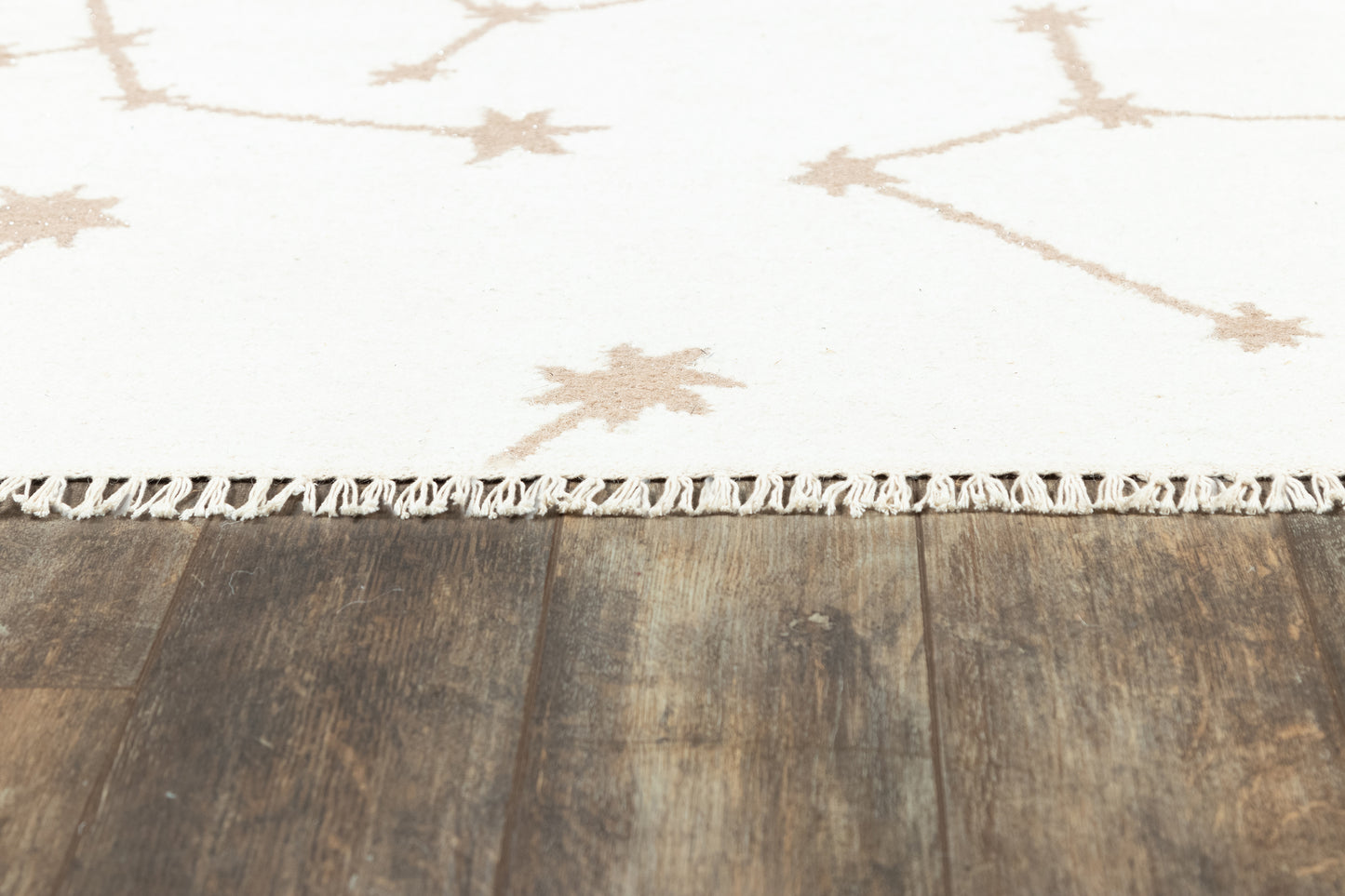 White rug with tan starburst motifs and fringe trim on dark wooden floor.