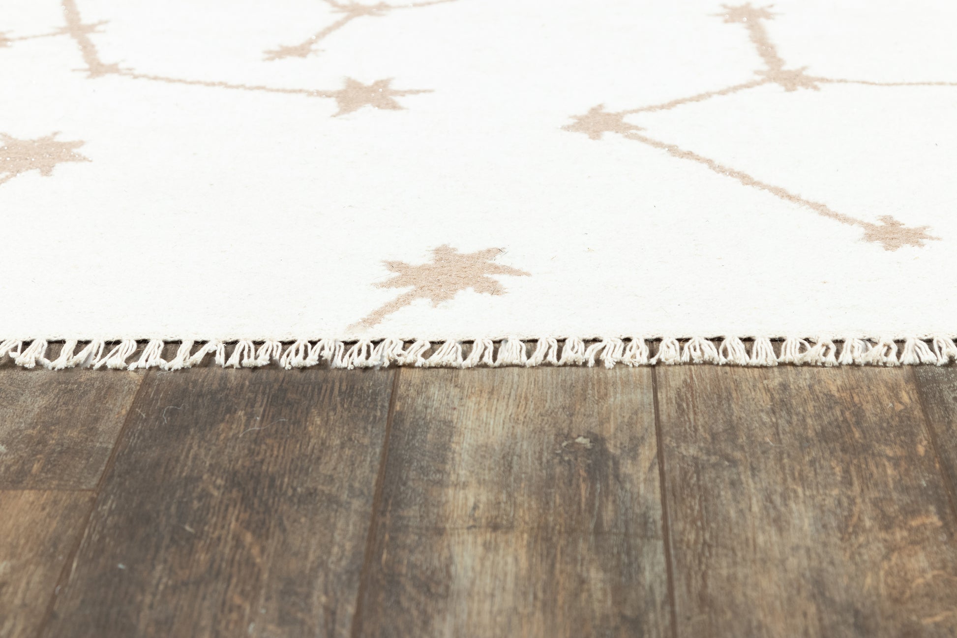 White rug with tan starburst motifs and fringe trim on dark wooden floor.