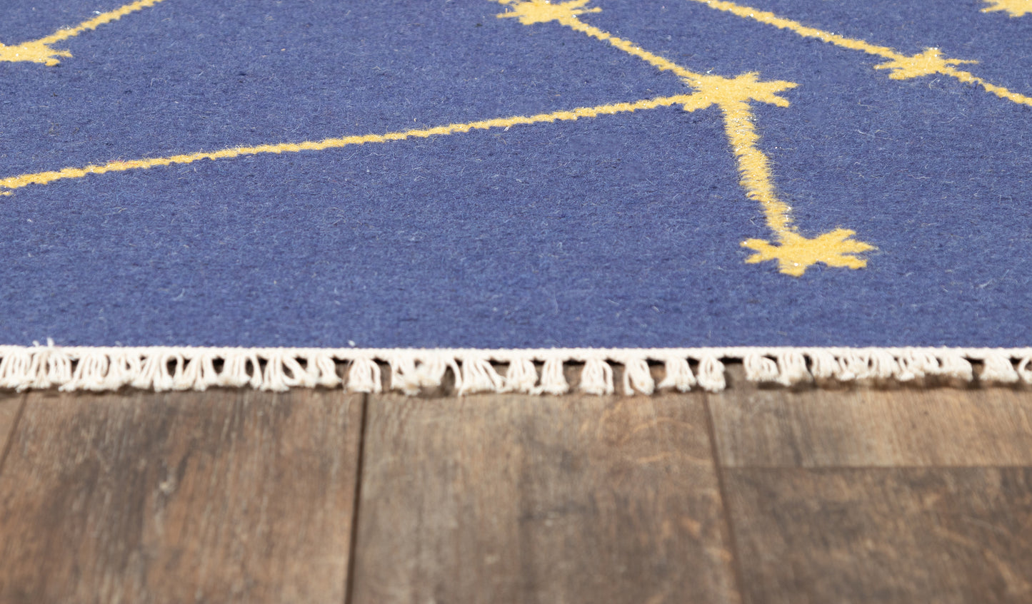 Blue rug with cream constellation pattern and white fringe edge on a wooden floor.