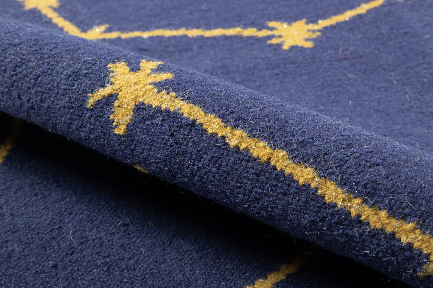 Navy blue rug with gold starburst motifs along a stripe; plush wool-like pile, folded edge.
