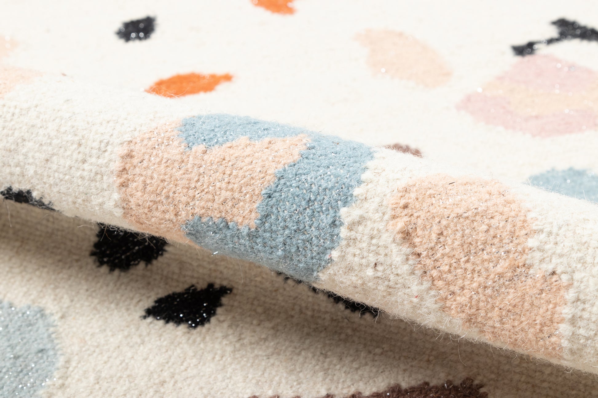 Cream woven rug with pastel blotches in peach, blue, tan, orange & black; soft textured pile and folded edge.
