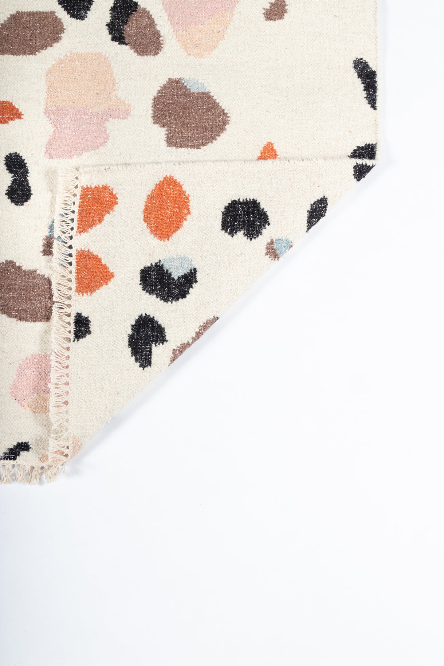 Beige rug with a colorful abstract leopard print in orange, pink, black and brown, with a folded corner and stitched edge.