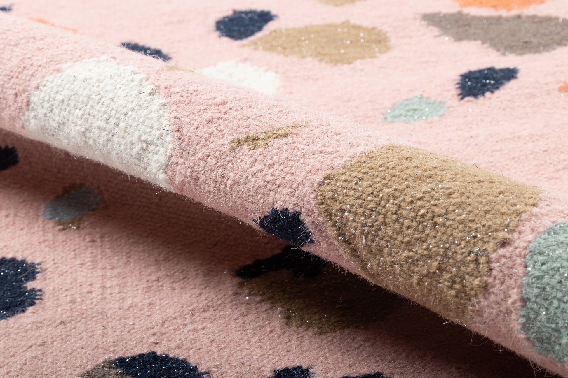 Pink fuzzy rug with scattered multicolor dots in navy, beige, teal, and white; plush texture with a folded corner.