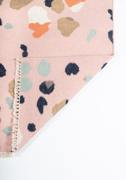 Pink woven rug with abstract multicolor blotches, fringe trim along the edge.
