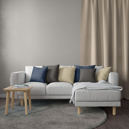 Light gray fabric sofa with chaise, blue/gray/beige cushions, beige throw, round wooden side table on a gray rug.