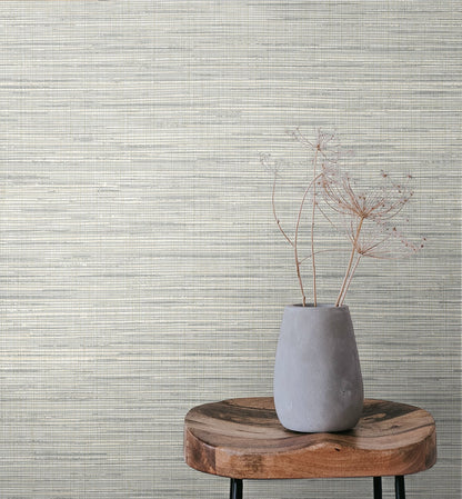 Gray ceramic vase with dried delicate stems on a round wooden slab against a textured beige wall.