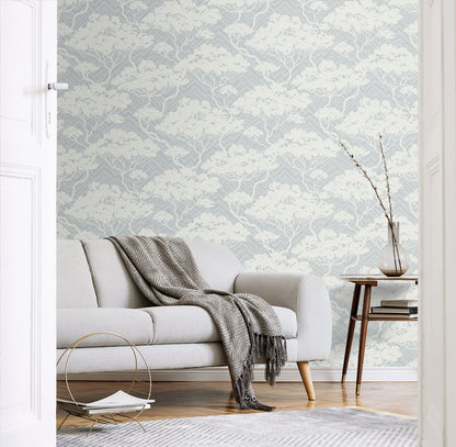 Light gray sofa with a knit throw in a blue-gray botanical wallpaper living room; wooden side table with a vase.