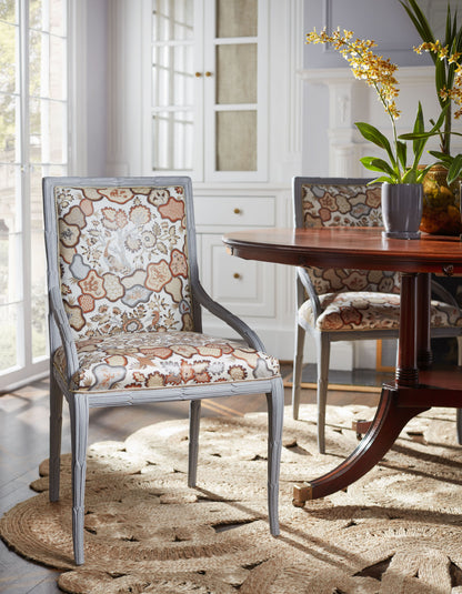 Grey wooden dining chair with cognac fabric upholstery, beside a round pedestal table in a bright dining room.