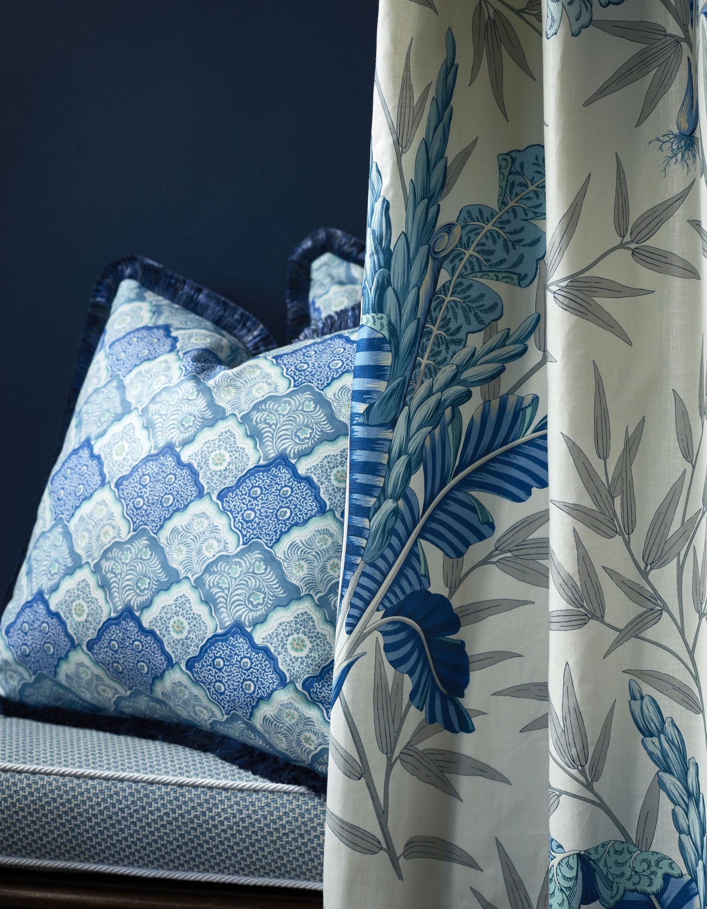 Blue botanical curtains with grey-blue foliage beside a blue-and-white patterned pillow on a navy upholstered chair.