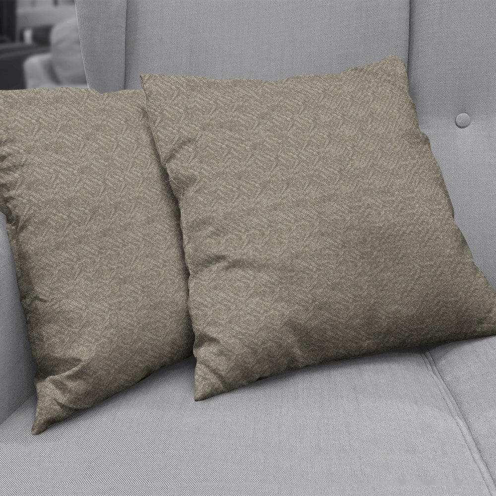 Two tan textured square throw pillows with a subtle geometric pattern on a gray sofa.