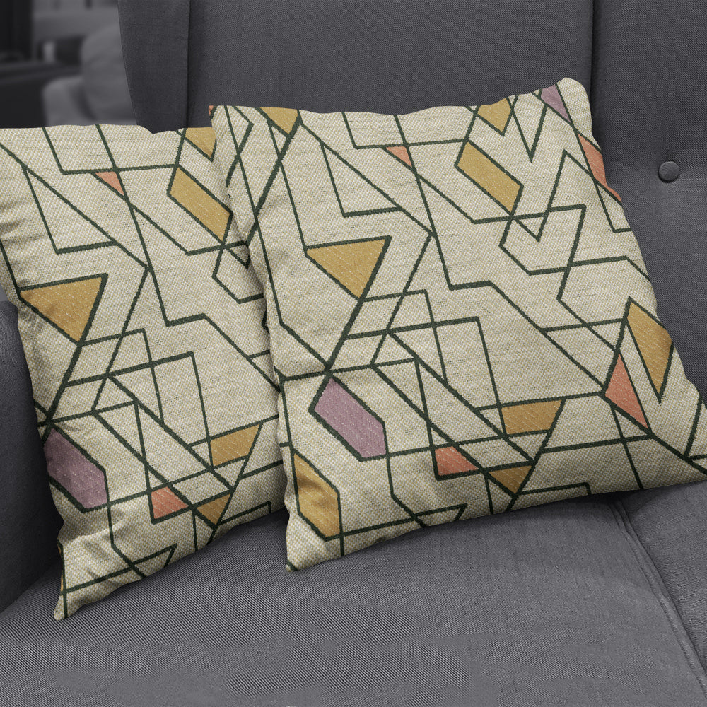 Two beige linen throw pillows with black geometric line art and yellow, pink, and green shapes on a gray sofa.