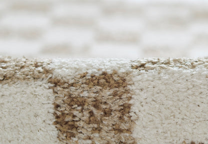 Beige plush rug with a brown stain patch and soft textured fibers for indoor flooring.
