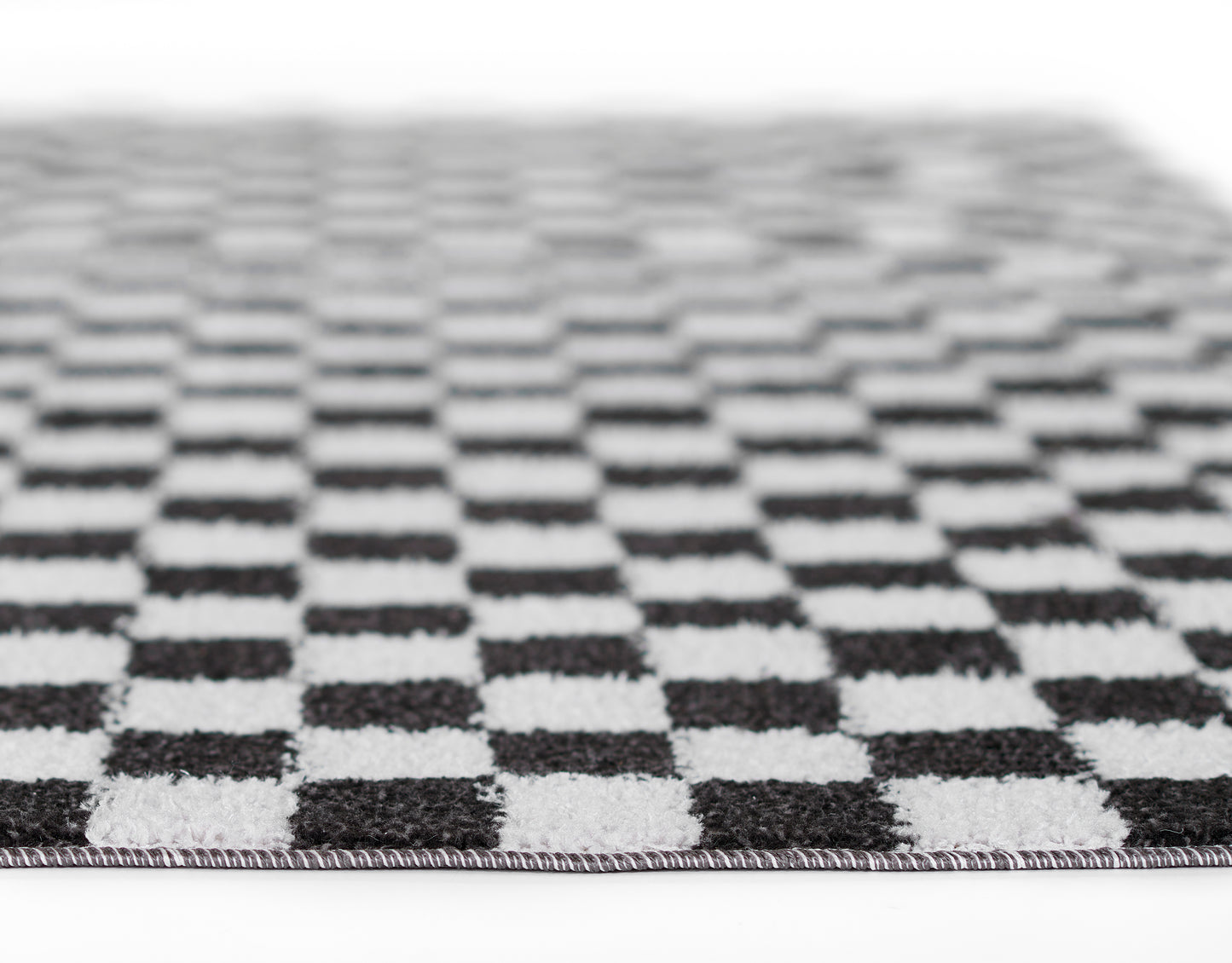 Black and white checkerboard rug with woven texture and fringe edge, rectangular.