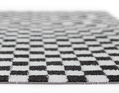 Black and white checkerboard rug with woven texture and fringe edge, rectangular.