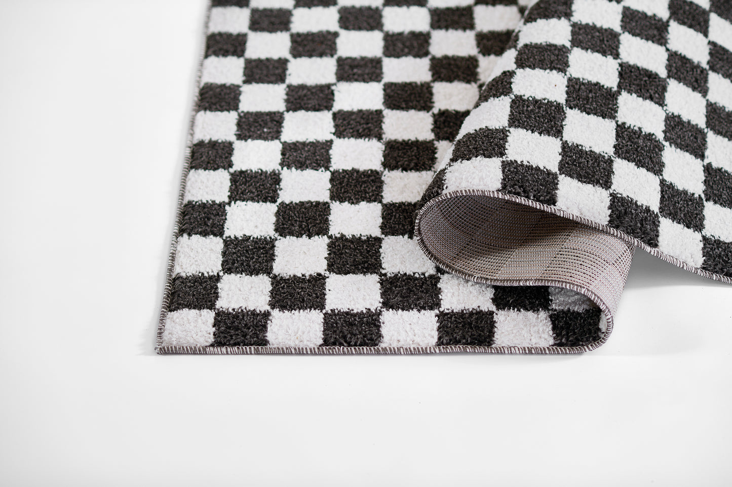 Black and white checkerboard rug with pink edging, folded at the corner.