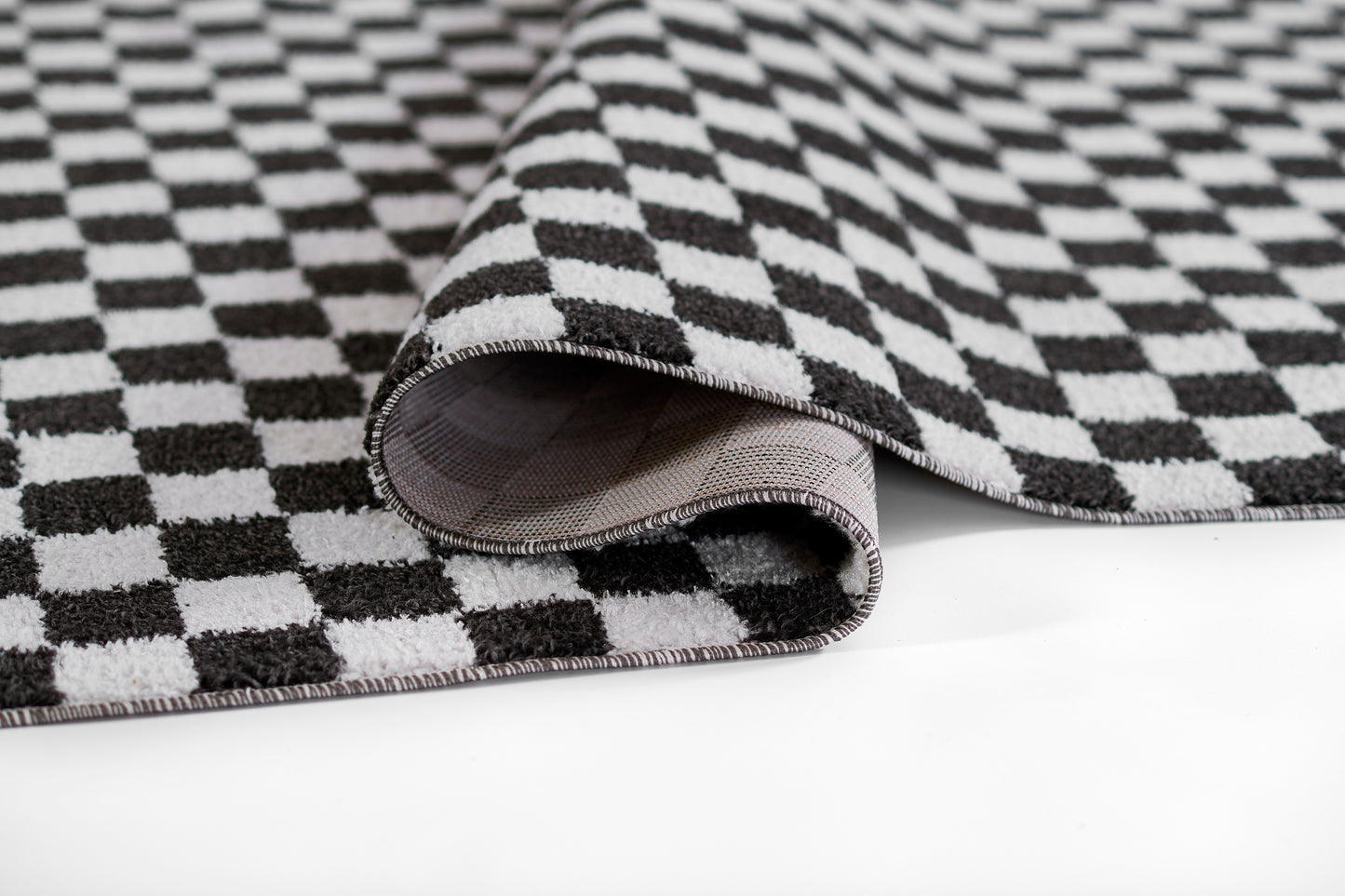 Black & white checkered fabric rug with folded edge, woven texture, modern geometric throw rug.