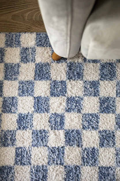 Blue & white checkered rug under a gray sofa; a small wooden sofa leg peeks out.