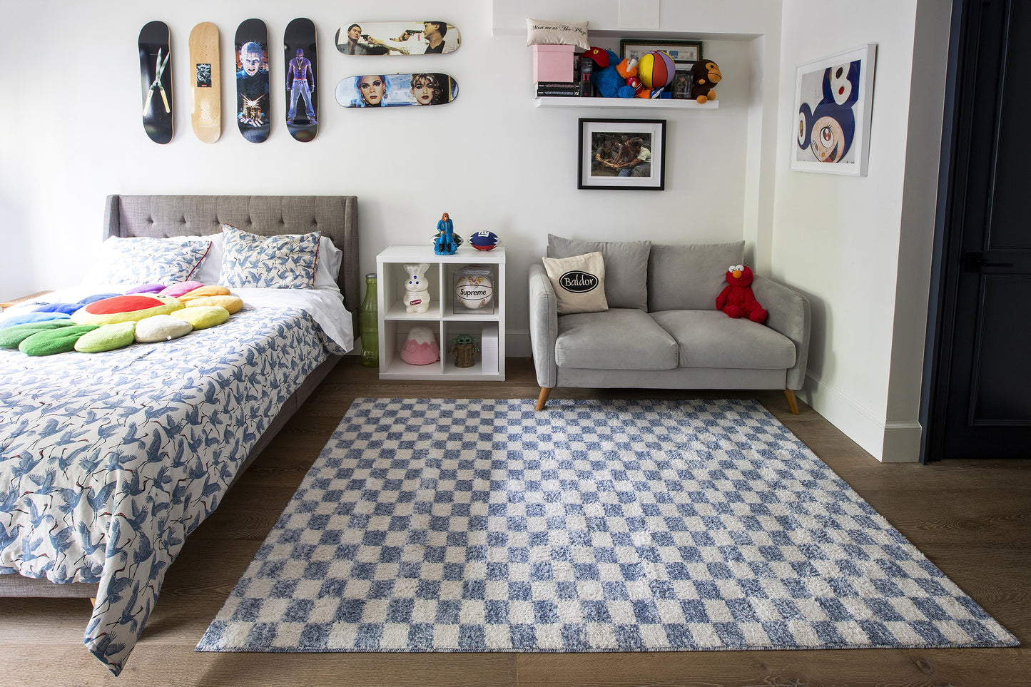Blue-and-white checkered area rug anchors a modern kids' bedroom with a gray loveseat, skateboard wall art, and cozy bedding.
