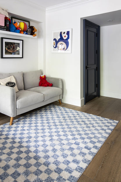 Light gray mid-century sofa with wooden legs, red stuffed toy, blue-white geometric rug, white walls, dark blue doorway.
