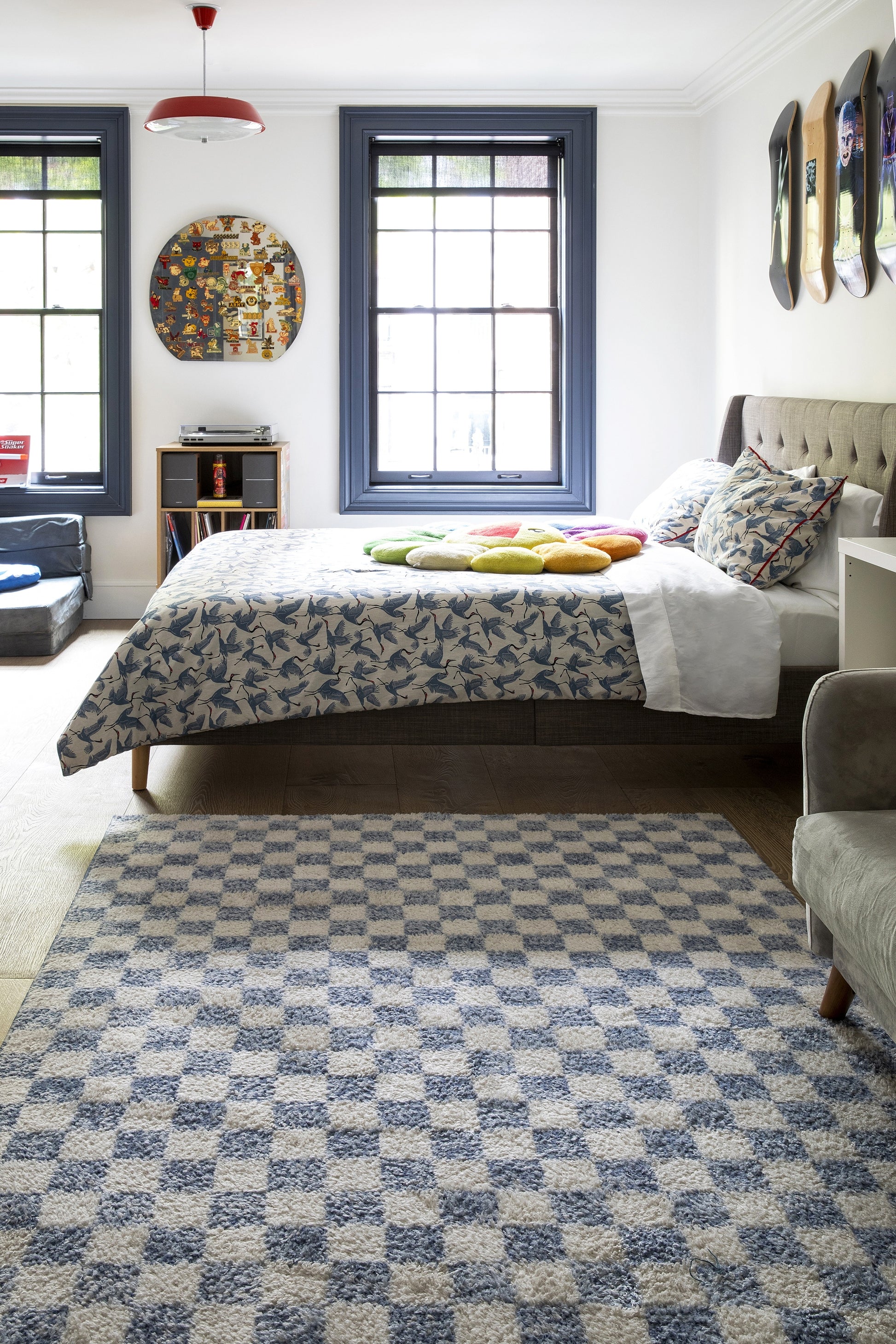 Blue floral bedspread on a tufted beige headboard bed in a bright bedroom with blue window frames.