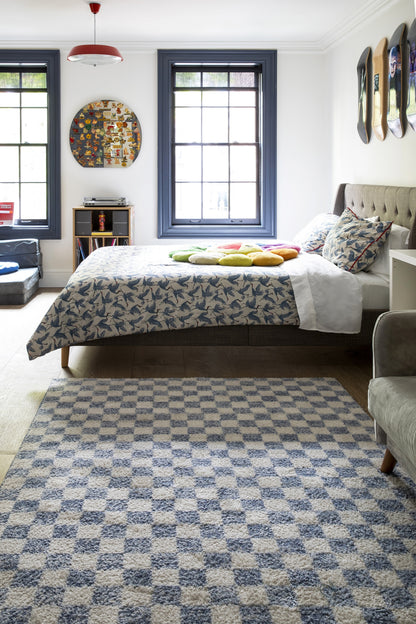 Blue floral bedspread on a tufted beige headboard bed in a bright bedroom with blue window frames.
