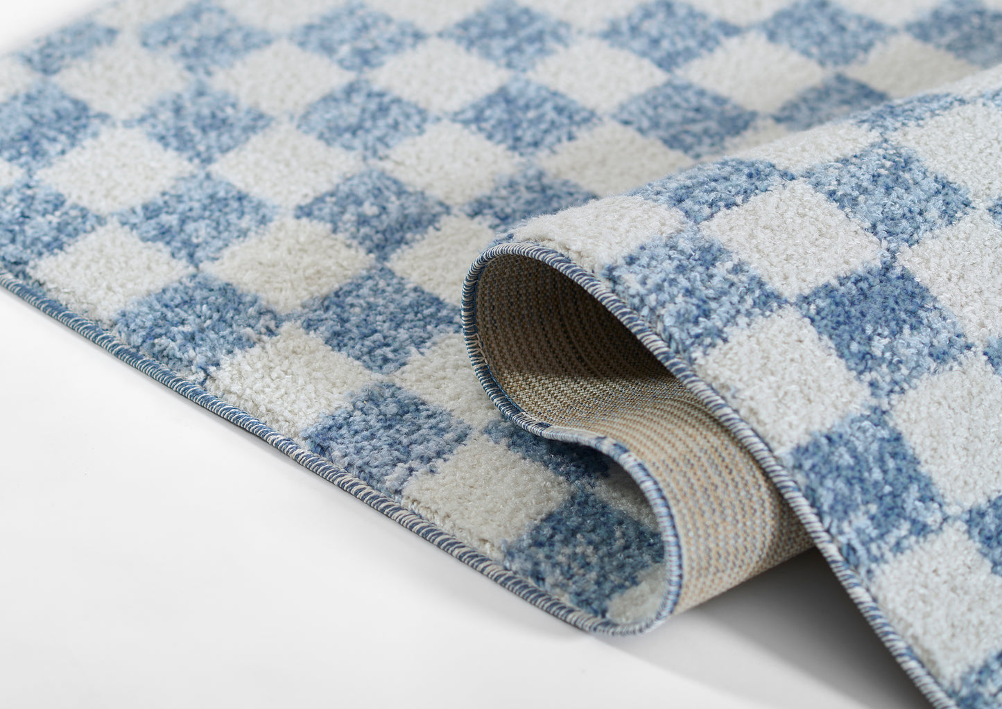 Blue and ivory checker rug with a soft plush pile; rolled edge reveals beige non-slip backing.