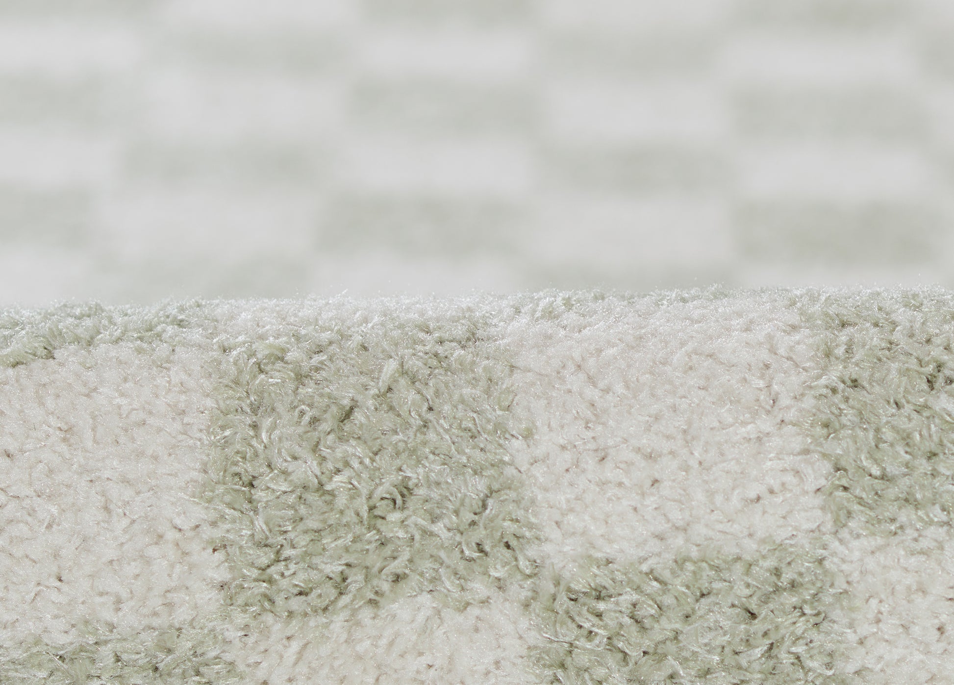 Close-up of a plush shag rug in cream and sage green blocks with a soft, fluffy pile.