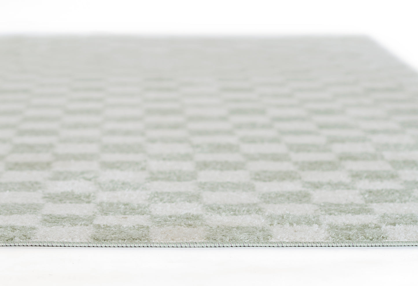 Close-up of a pale green and ivory checkered rug with soft woven texture and slim edge binding.