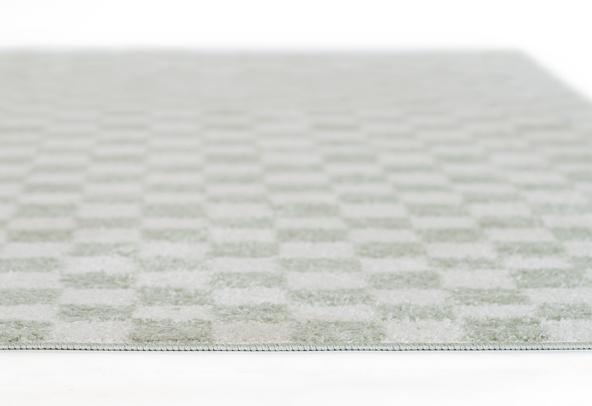 Close-up of a pale green and ivory checkered rug with soft woven texture and slim edge binding.