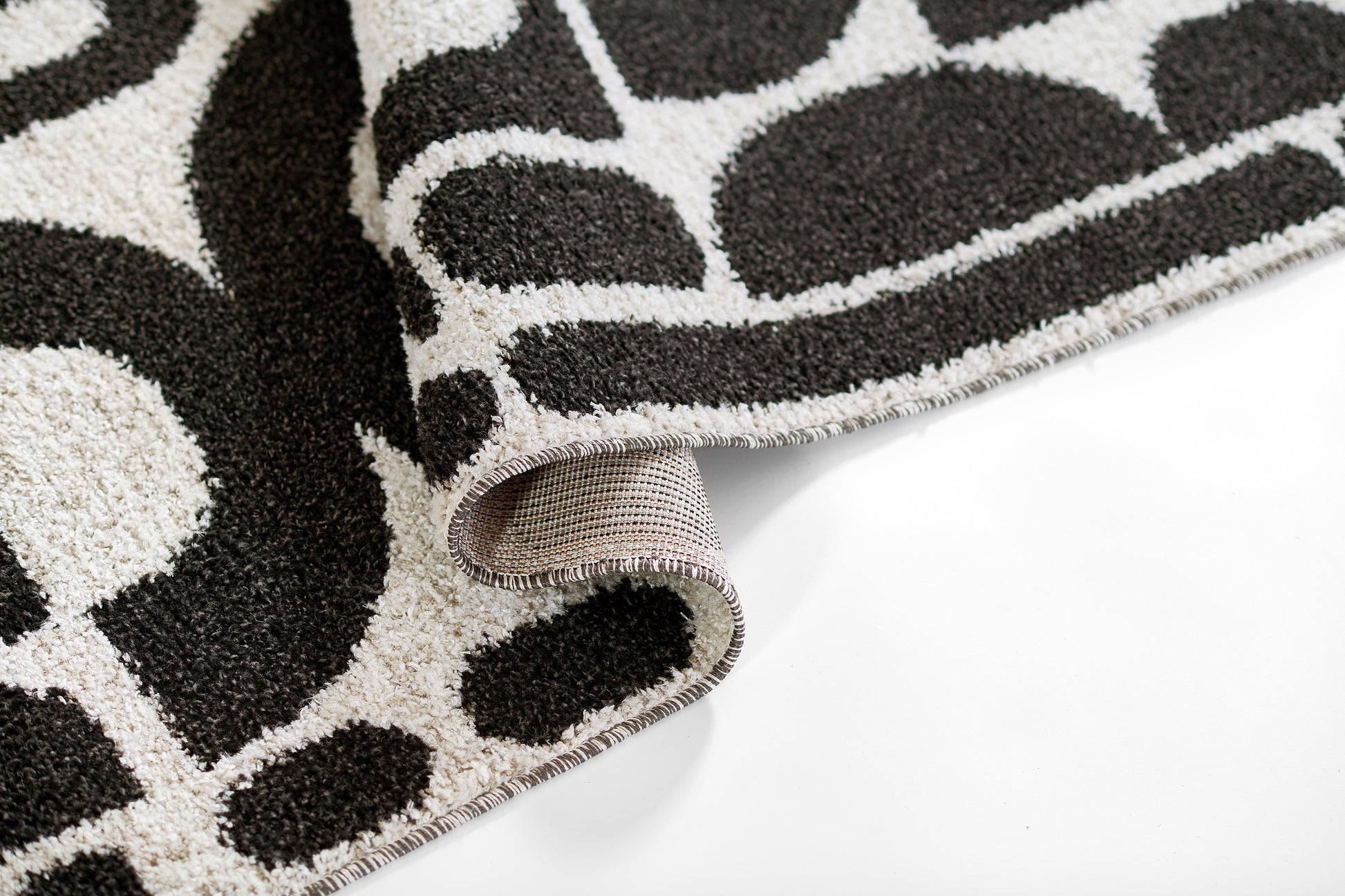 Close-up of a black and ivory loop-pile rug with bold abstract shapes, rolled edge.
