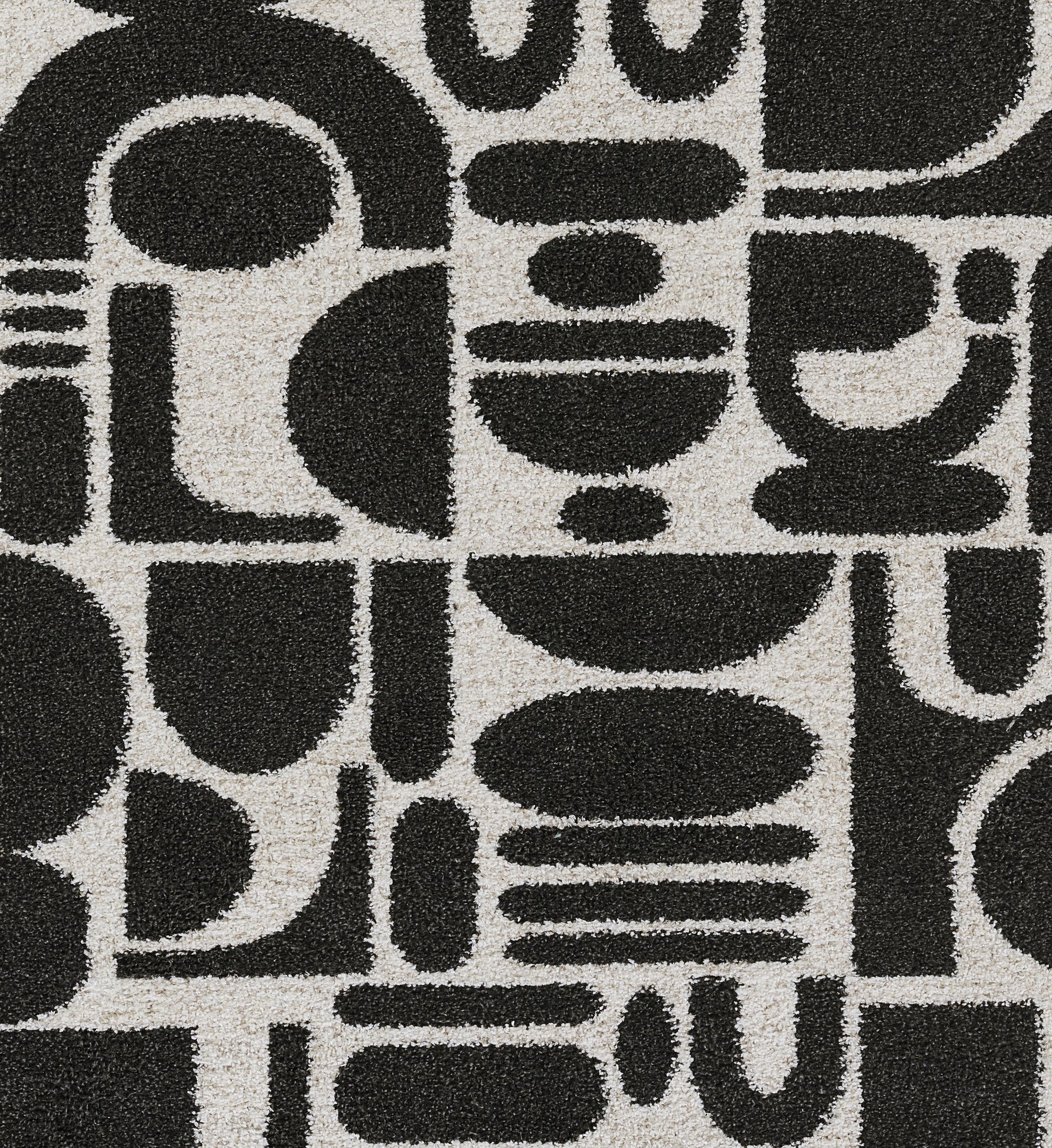 Beige rug with bold black geometric shapes forming square tile pattern; abstract mid-century style.
