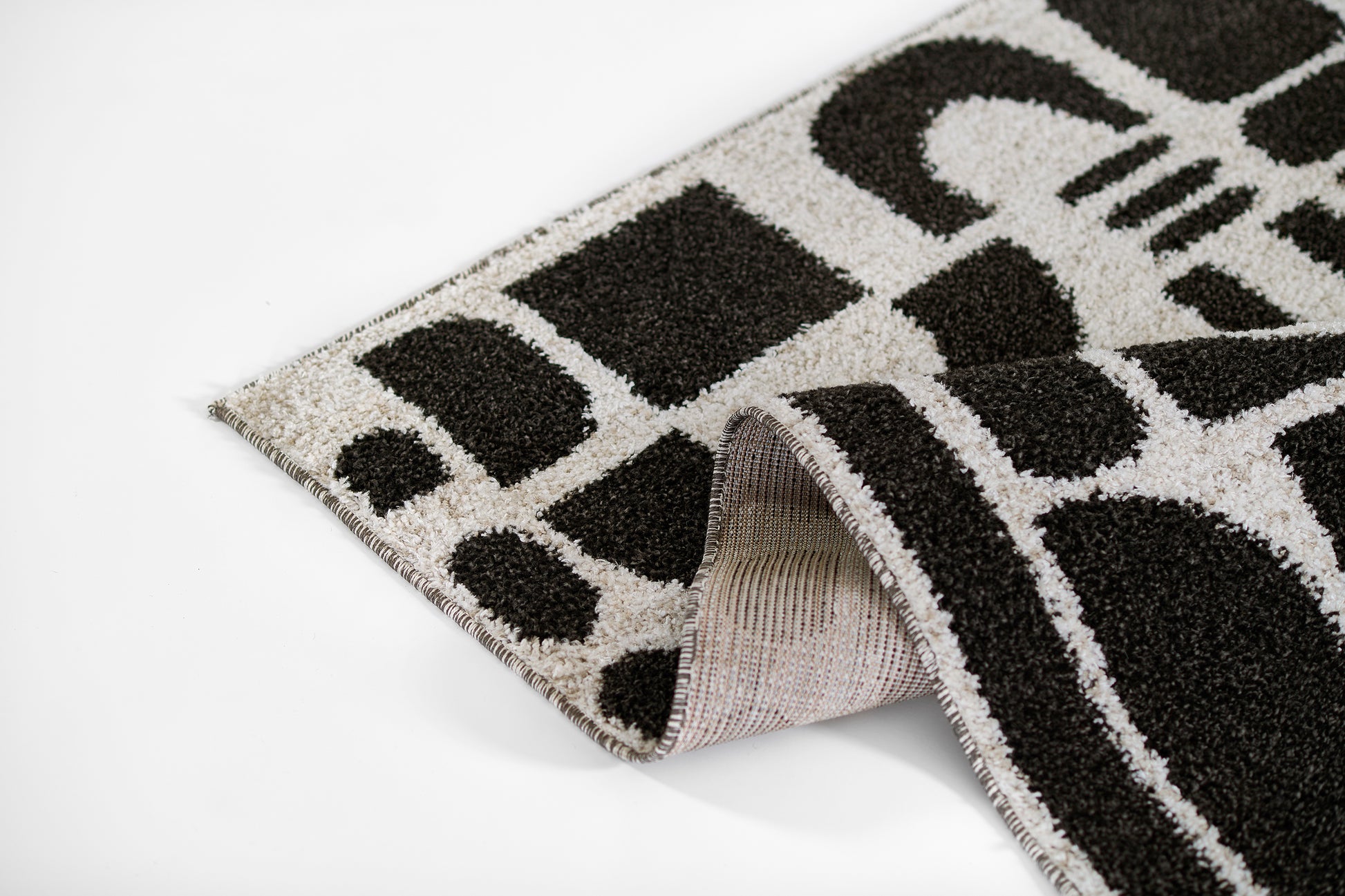 Black and white geometric rug with loop pile; folded corner reveals beige underside.