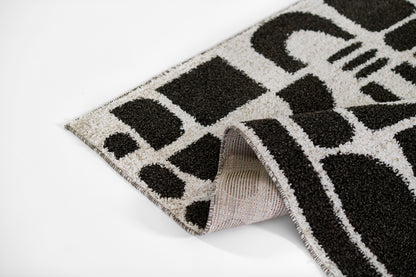 Black and white geometric rug with loop pile; folded corner reveals light beige underside.