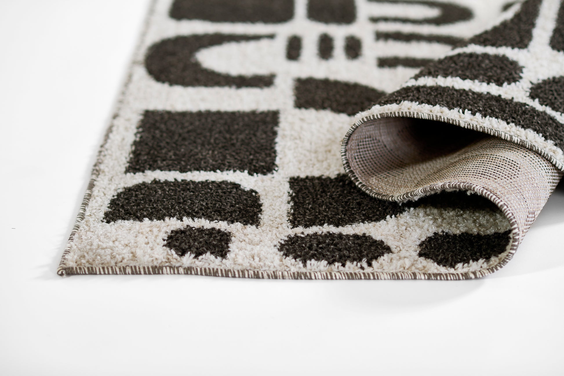 Rolled black and ivory geometric rug with fringe, modern woven design for living spaces.