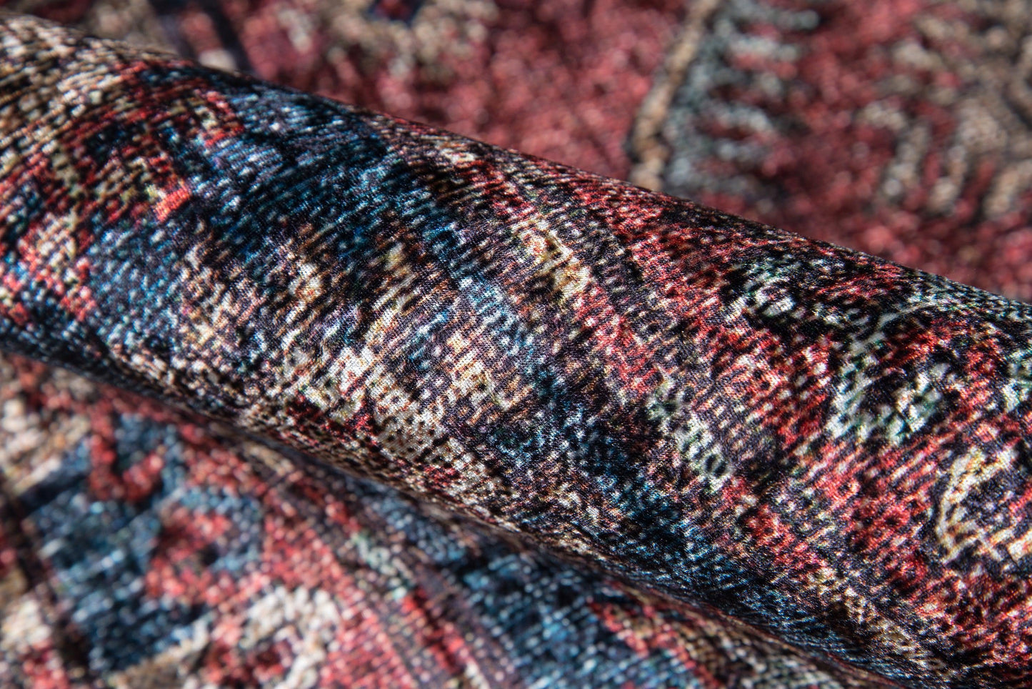 Close-up of rolled multicolor wool rug with burgundy, navy, and cream tones and ornate pattern.