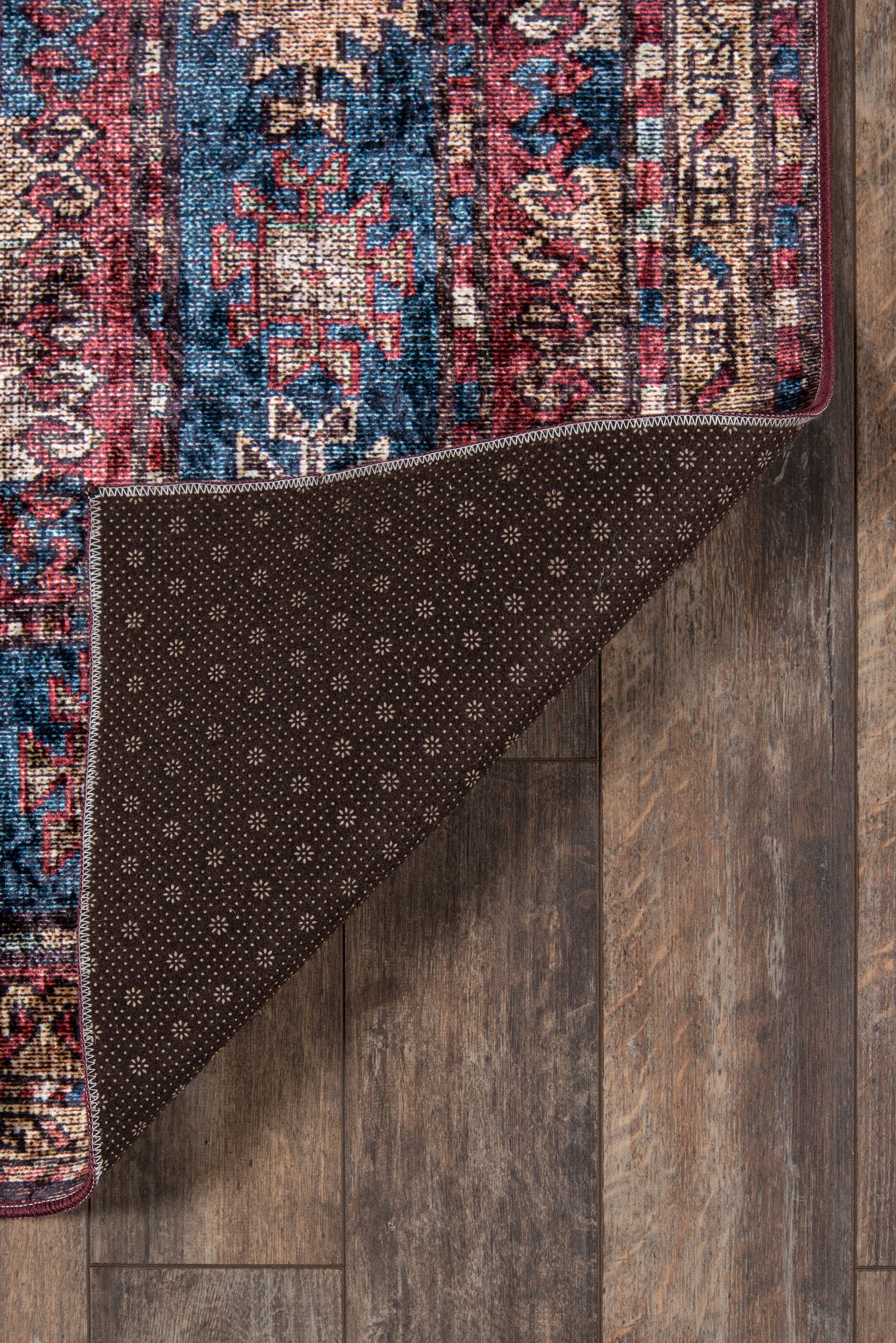 Persian-pattern area rug in red, blue and cream; folded corner reveals brown dotted backing on wood floor.