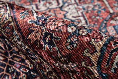 Close-up of a red Persian-style rug with blue and cream floral motifs and a folded edge.