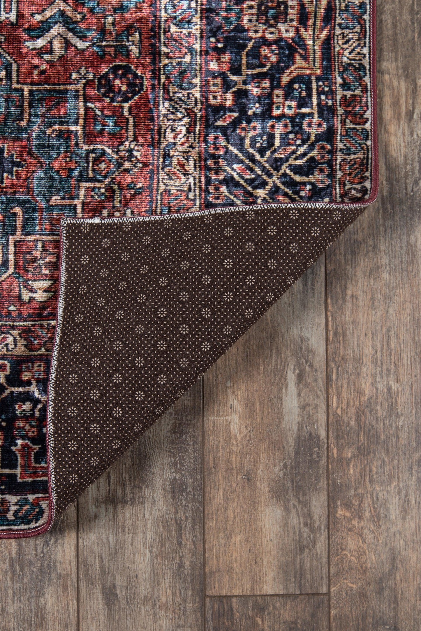 Red & navy oriental rug with floral motifs, folded at corner to reveal brown dotted backing on wooden floor.