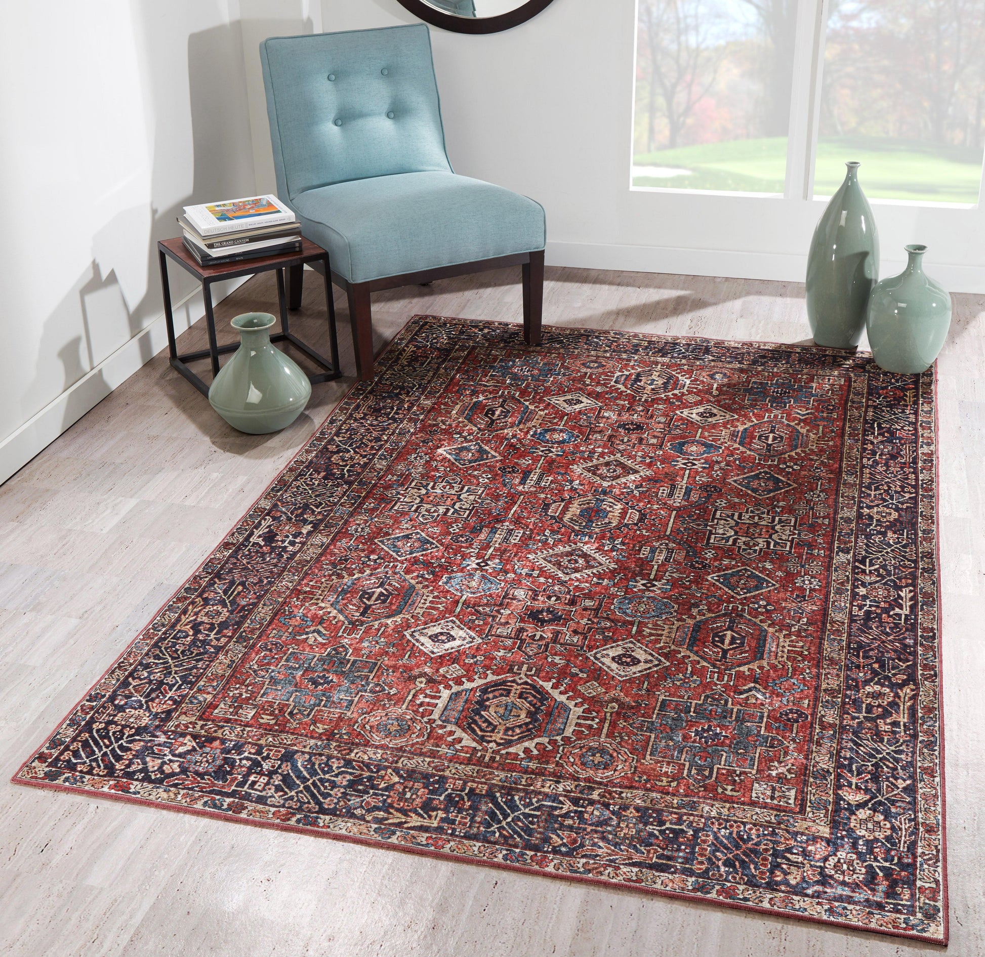 Red and navy Persian-style area rug with intricate pattern on light wood floor, beside a teal chair and green ceramic vases.
