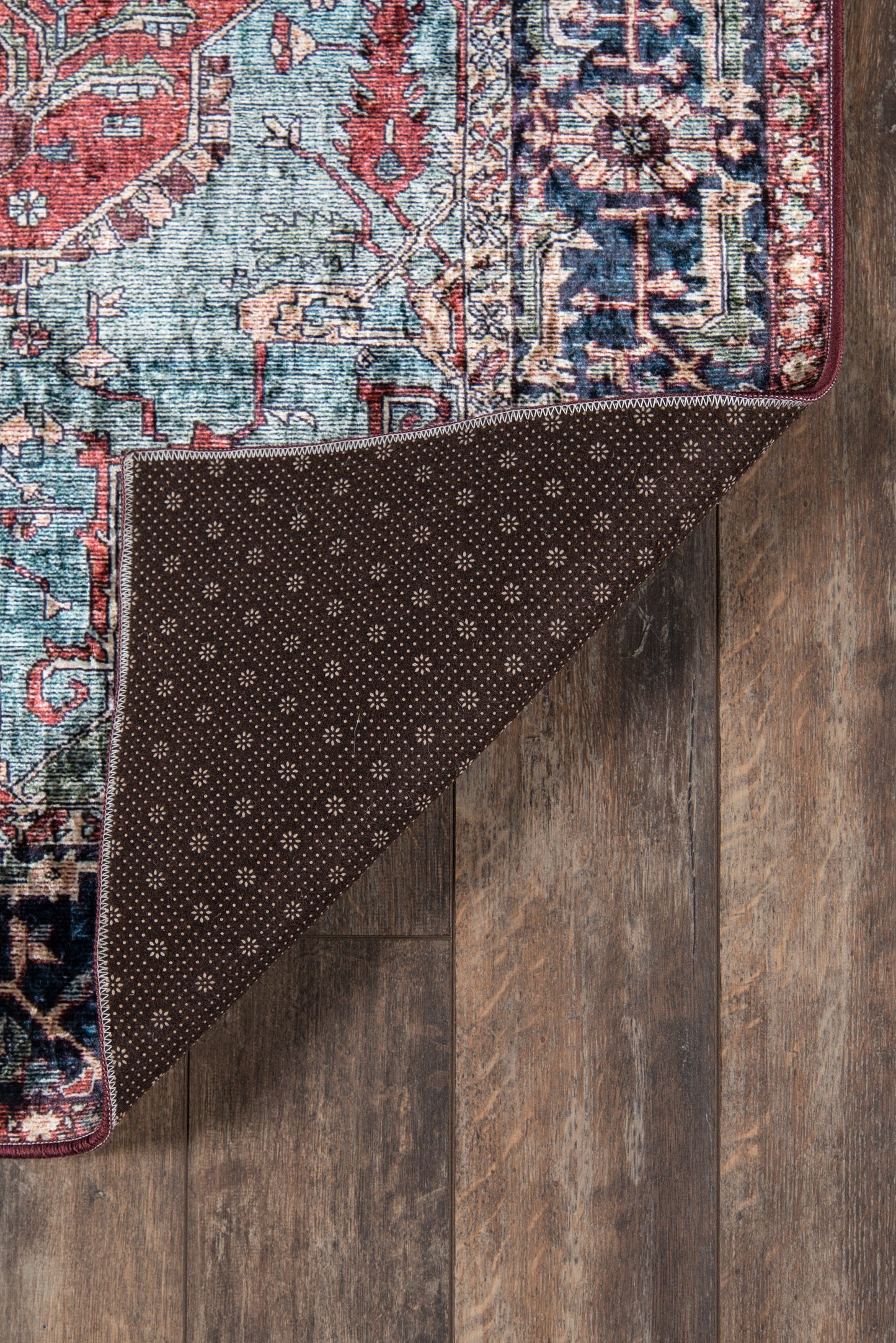 Traditional oriental rug with teal, red and ivory pattern; corner folded to show dark brown dotted underside on wood floor.