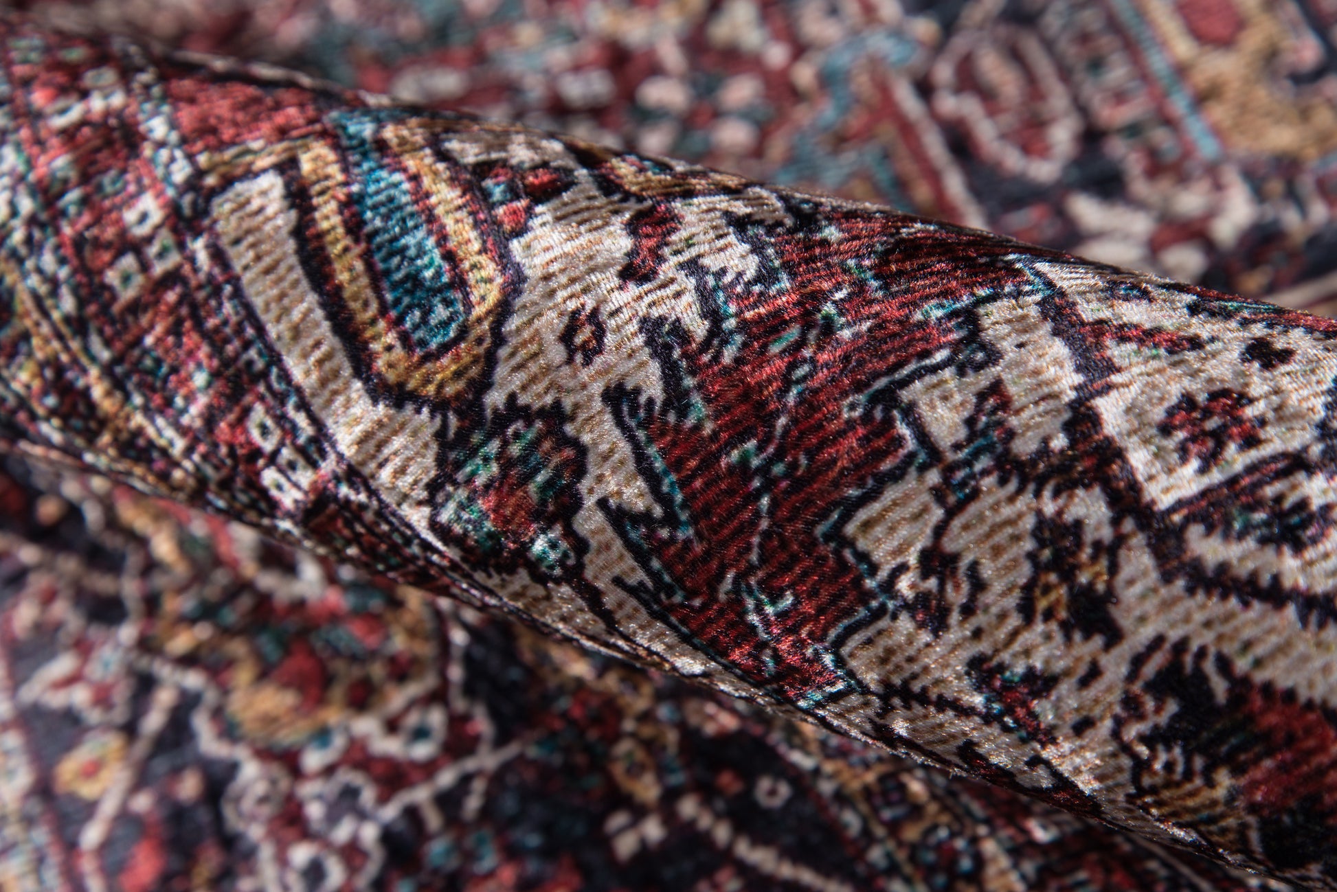 Rolled Persian-style rug with red, ivory & teal floral patterns and dense oriental motifs.